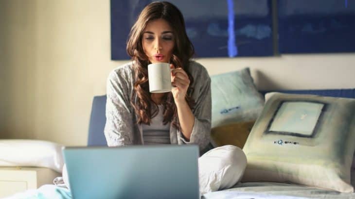 woman drinking coffee in bed with the computer