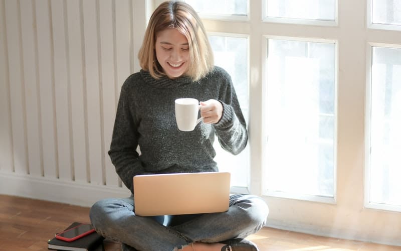 a woman sitting on the ground with a laptop and coffee
