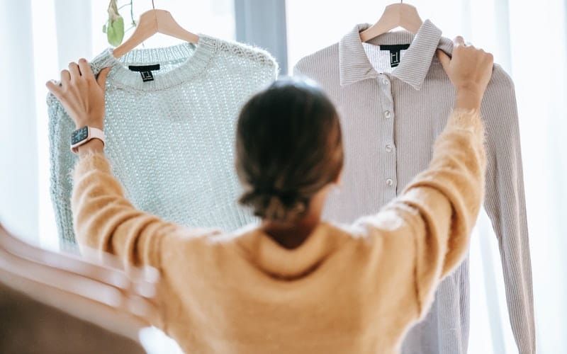 a woman holding two shirts on hangers