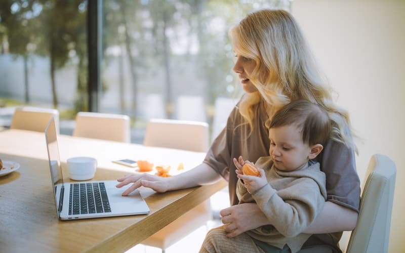 a woman holding a child while using a laptop