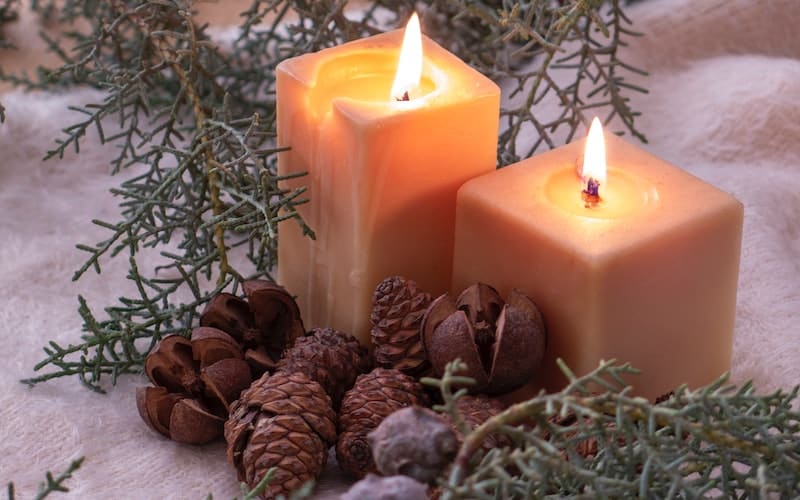 two lit candles near boughs of fir and pinecones